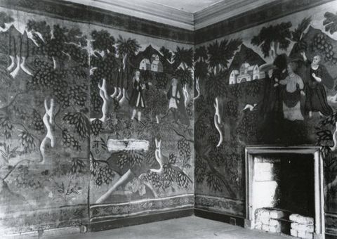 Textile. Black and white photograph of the corner of a room hung with cloth shows a landscape scene with people and buildings.