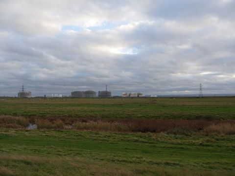 A flat grassland leads to factory buildings and pylons along the horizon.