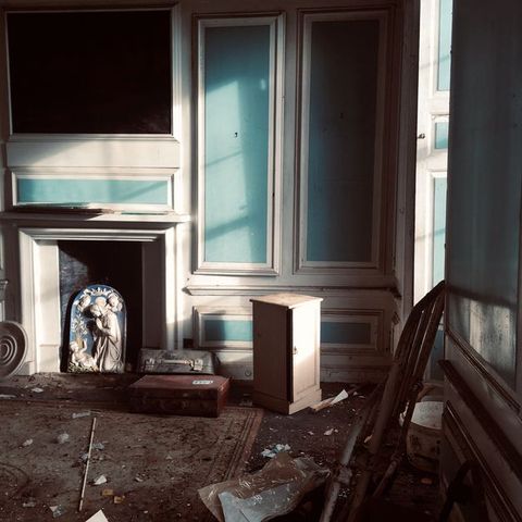 Architecture. A shadowy corner has turquoise-blue and white panelling. Debris is scattered around the floor and around an arch-topped blue and white porcelain panel showing the Virgin Mary adoring the Christ child.