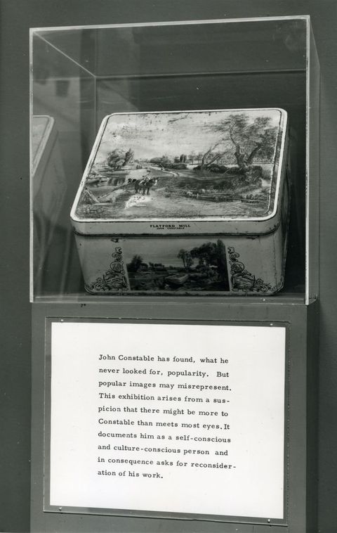 Installation. Black and white image of a tin box illustrated with a landscape scene in an exhibition case. Wall text below reads, “John Constable has found, what he never looked for, popularity. But popular images may misrepresent. This exhibition arises from a suspicion that there might be more to Constable than meets most eyes. It documents him as a self-conscious and culture-conscious person and in consequence asks for reconsideration of his work”.