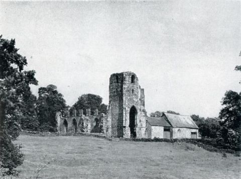 Black and white photograph. The ruins of a tower and priory are across a grassy expanse.