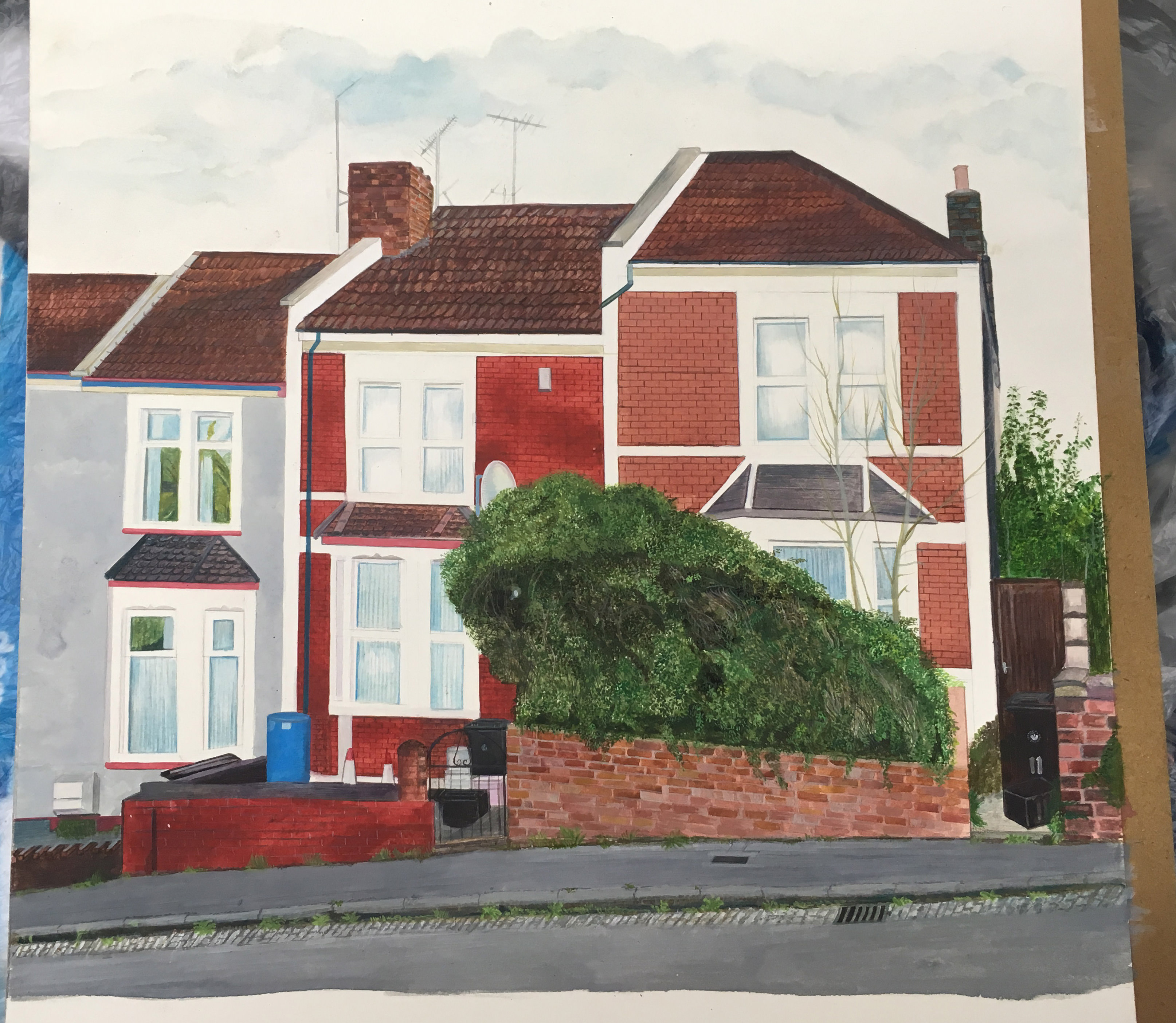 Watercolour. Three rowhouses descending along a road fill this composition. The leftmost structure is smoke grey. The other two are red brick. An alleyway runs alongside the rightmost house. A brick retaining wall in front of that house is filled with an overgrown hedge, which nearly covers the bay window at the front.