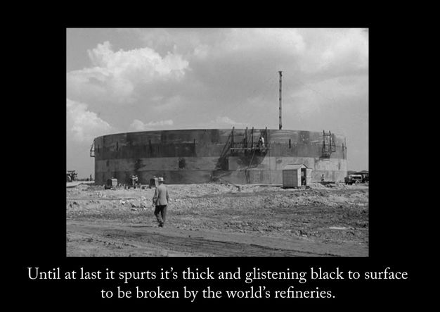 Film still. Black and white image of a circular building on a dirt ground. Below the photo, white text is set against a black background. Text reads, “Until at last it spurts it’s thick and glistening black to the surface to be broken by the world’s refineries”.