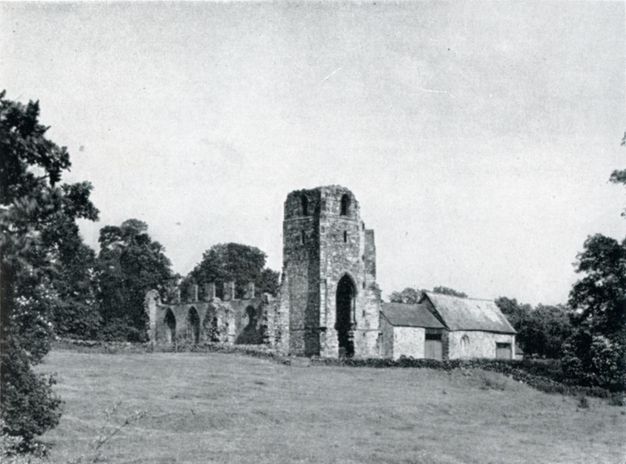 Black and white photograph. The ruins of a tower and priory are across a grassy expanse.