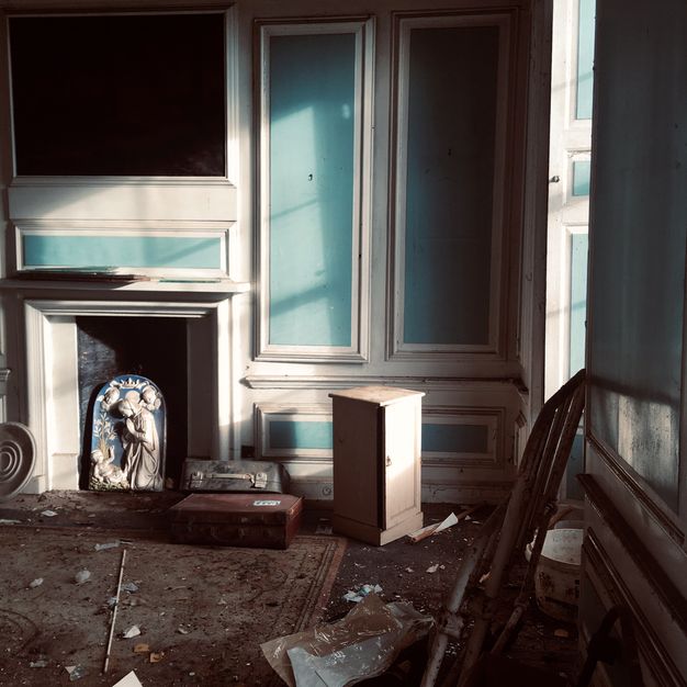 Architecture. A shadowy corner has turquoise-blue and white panelling. Debris is scattered around the floor and around an arch-topped blue and white porcelain panel showing the Virgin Mary adoring the Christ child.