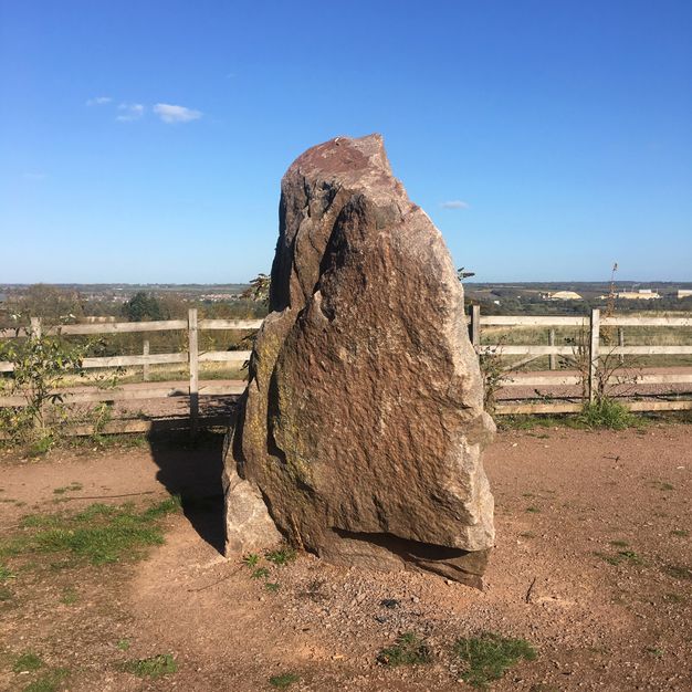 A triangular stone rises like an incisor in a dirt field.