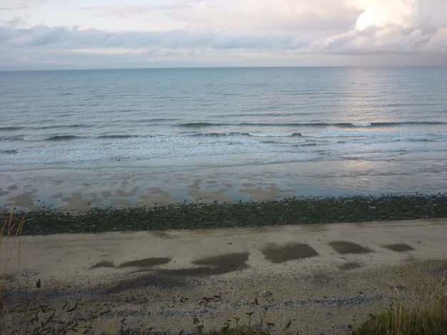 We look down onto a strip of sandy beach stretching across this photograph. The far side is lined with rocks and then the rows of breaking waves.