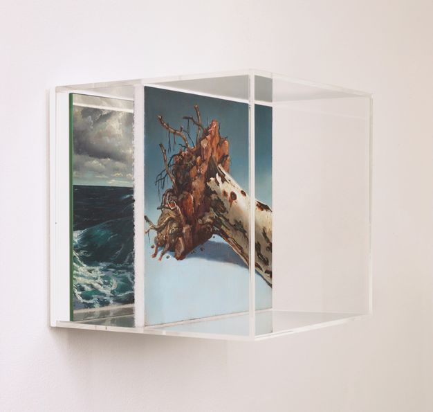 Sculpture. A perspex cube is mounted on a wall so that it projects towards us. A square panel is mounted halfway inside the cube. On the side of the panel facing us is a painting of an uprooted tree against a blue background. Inside the cube, against the wall, is a mirror in which the back of the panel is reflected. On the back of the panel is a painting of a dark seascape with breaking surf.