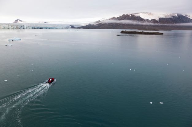 A motorized boat heads for a rocky island near ice floes and mountains in the distance.