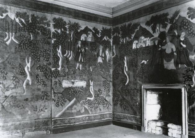 Textile. Black and white photograph of the corner of a room hung with cloth shows a landscape scene with people and buildings.