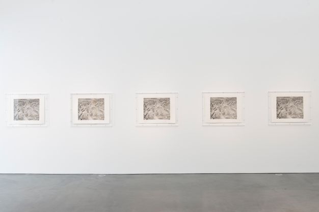 Installation. Five silvery black and white photographs are contained in acrylic boxes hung on a gallery wall. The images show a mine.