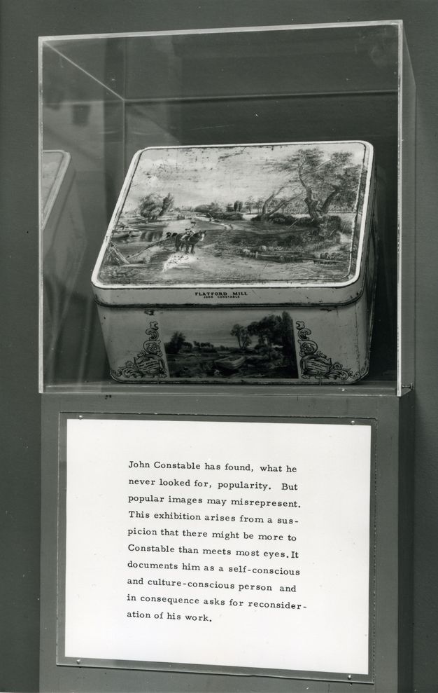 Installation. Black and white image of a tin box illustrated with a landscape scene in an exhibition case. Wall text below reads, “John Constable has found, what he never looked for, popularity. But popular images may misrepresent. This exhibition arises from a suspicion that there might be more to Constable than meets most eyes. It documents him as a self-conscious and culture-conscious person and in consequence asks for reconsideration of his work”.