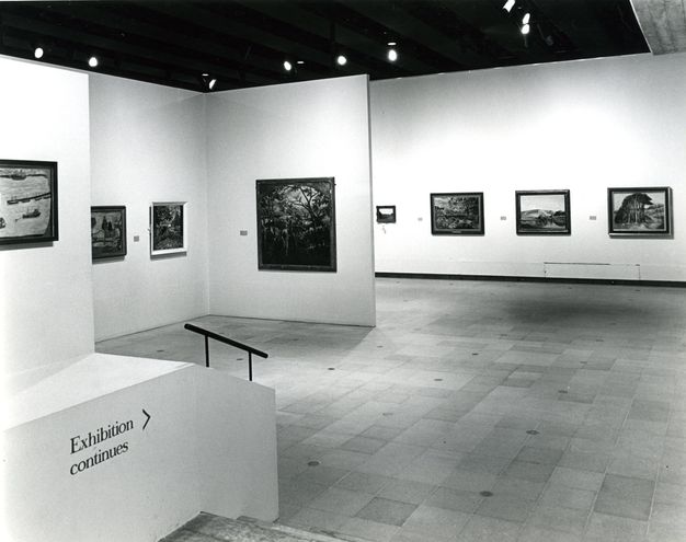 Installation. Black and white photograph shows eight paintings hung widely spaced along white walls.