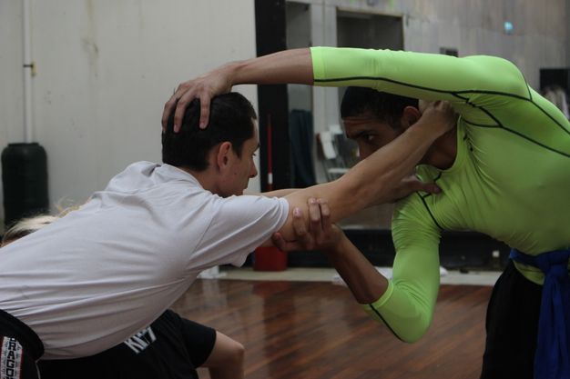 Colour photograph. Two dancers reach, leaning towards each other and holding onto each other’s heads, necks, and shoulders.