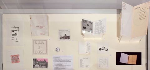 Installation. Fourteen works on paper, images, or books are displayed in a case.