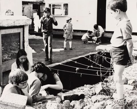 Black and white photograph. Nine children are around or in a trench in a courtyard.
