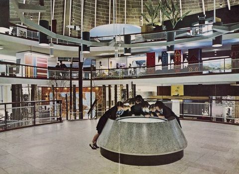 Installation. Seven people gather around the round surface of a light table at the centre of a three-storey atrium.