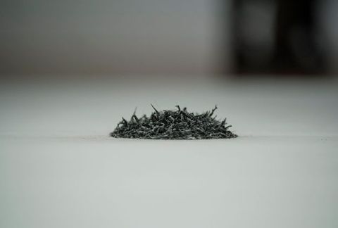 Installation. Close up view of a pile of grey rubber eraser shavings. The space behind the pile quickly falls out of focus.