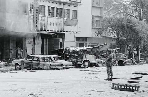 Black and white photograph. Two uniformed soldiers stand on a street lined with burned-out cars and buildings.