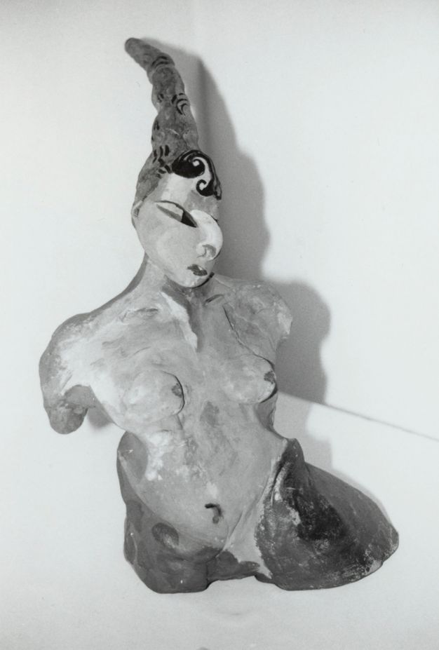 Sculpture. Black and white photograph of the torso and head of a stylized woman. A thin cone-like hat or headdress is over dark hair. Some of her features are exaggerated, like a curving, half-moon nose.