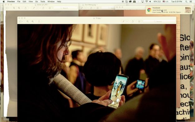 Screenshot. An image of a person taking a picture in an art gallery is at the front of windows layered on a computer desktop. The person looks at his phone, finger poised to take the picture, which is of a woman wearing a yellow suit and reading from a piece of paper.