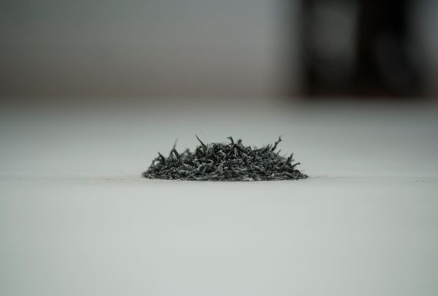 Installation. Close up view of a pile of grey rubber eraser shavings. The space behind the pile quickly falls out of focus.