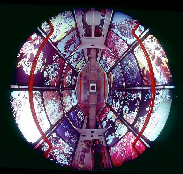 Installation. A round, disorienting space is given some direction when we find a person standing at double doors at the bottom centre of the circle. This suggests we look up into a space from under a glass floor. The walls are covered with floral and decorative patterns.