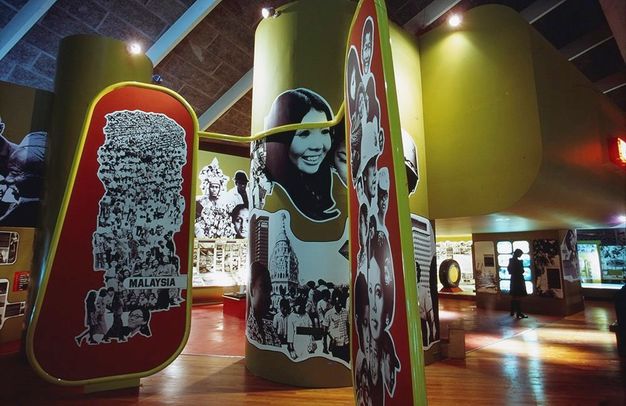 Installation. Black and white photographs are cut up and applied to red panels that nearly span floor to ceiling, or lime-green columns and walls, like giant stickers. The pictures we can see here are of people, either close up or in huge crowds.