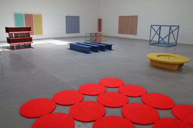 Installation. Colourful discs and objects making patterns are on the floor or gallery walls in this exhibition space.
