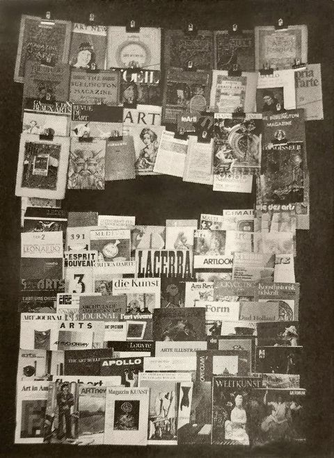 Illustration. Black and white photograph of about seventy journal covers, some clipped to wires across the top and others stacked below. Titles are in English, German, and French, among others.