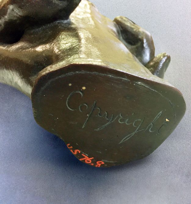 Sculpture. We look at the flat, oval end of a bronze sculpture. Below the incised inscription, an accession number is written in red: “US 79.8”.