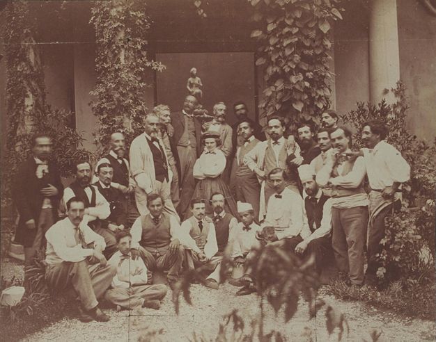 Black and white photograph. A woman is surrounded by twenty-four men in a courtyard.