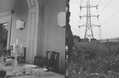 Black and white images. To our left, we look across a dining table set with plates and glasses at the wall of the room. To our right, power lines march back from a meadow of grasses and flowers.
