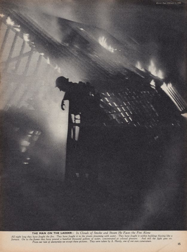 Magazine illustration. A man with a brimmed helmet leans out over a ladder against a burning building. The scene is shrouded in smoky haze. After the title, the caption below continues, “In Clouds of Smoke and Steam He Faces the Fire Alone”.