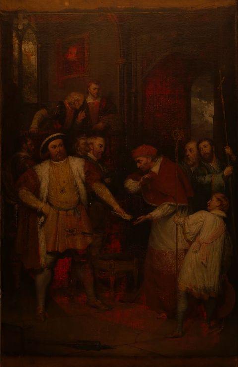 Painting. A man, Henry VIII, stands with feet widely planted, one hand on his hip as he hands a piece of paper to Thomas Wolsey, who wears red cardinal’s robes. The tones are dark and shadowy except where the red glows as the canvas is lit from behind.