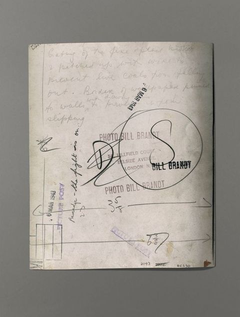 The back of a photograph has writing, measurements, and five different stamps with the date or name of the artist.
