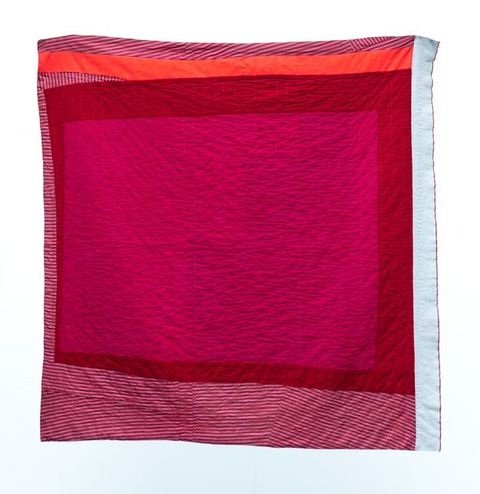 Quilt. A block of magenta pink is surrounded first by uneven bands of crimson red. Then white-and-red striped fabric, all white, or coral orange fill out the square in freeform strips.