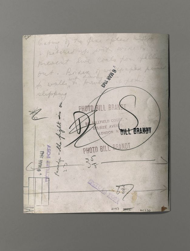 The back of a photograph has writing, measurements, and five different stamps with the date or name of the artist.