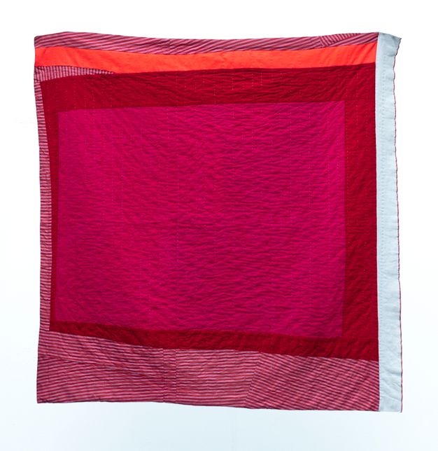Quilt. A block of magenta pink is surrounded first by uneven bands of crimson red. Then white-and-red striped fabric, all white, or coral orange fill out the square in freeform strips.