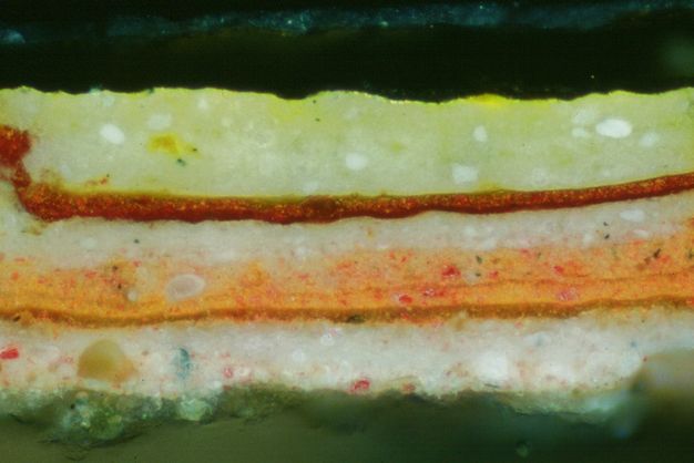 Microscopic cross section of paint. From the bottom up, layers are pine green, white, marigold orange, rust red, and lemon-lime flicked with white.