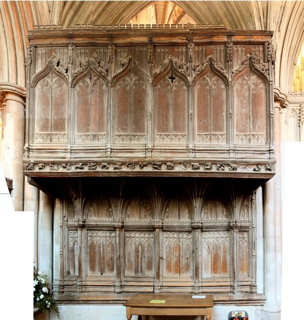 Architecture. A wooden watching loft, like a balcony, is built between two columns. The face on the top of two levels is carved with pointed arches lined on the outer edge with leafy decorations. The lower level is set back.