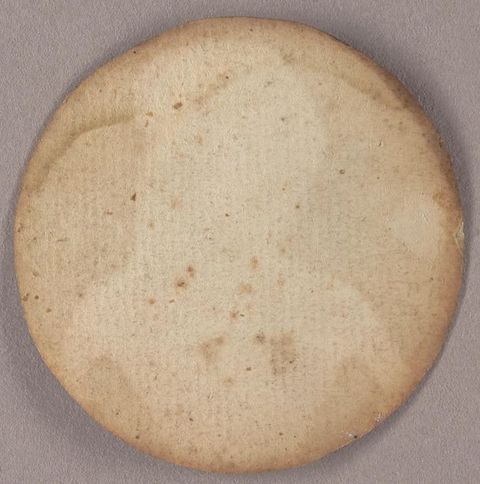 View of the back of a round portrait painting, which has been affixed to paper, now yellowed and water stained across the top. The outline and shape of the woman on the other side is visible.