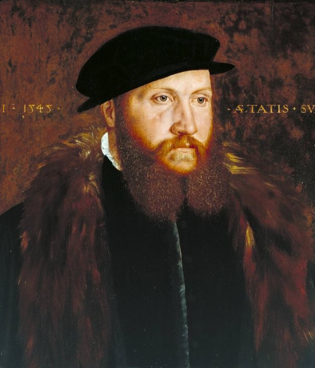 Painting. Shown from the chest up, a pale-skinned man with a ginger moustache and two-lobed beard looks off to our right. His cheeks are a little puffy with age under clear grey eyes. He wears a black cap and a brown fur wrap over a black jerkin.