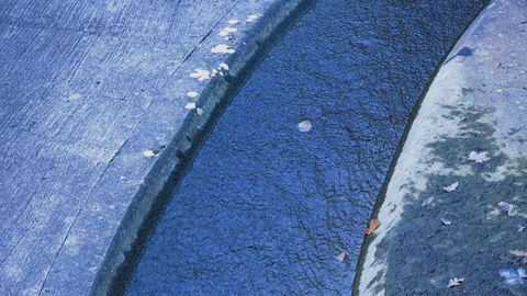 Video still. We look straight down onto what appears to be a slightly curving canal or aqueduct filled with lapis-blue water. Cement embankments line each side in paler shades of blue.
