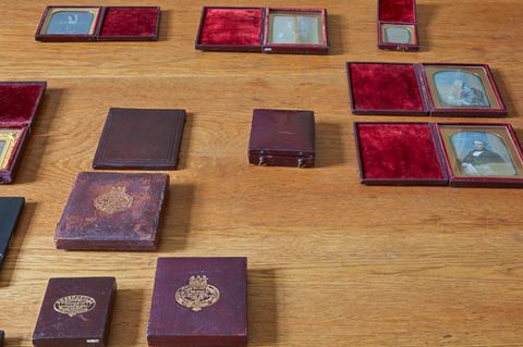 Colour photograph. Six daguerrotype portraits in fabric-lined, open cases along with five closed cases are arranged on a wooden tabletop. Light reflects off the glass fronts of the open photographs.