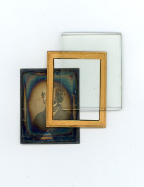 Colour photograph. Three parts of a framed daguerreotype are shown. The photograph has iridescent rainbow edges and is accompanied by a gold mat and a piece of glass to show how the photograph can be protected in a case.