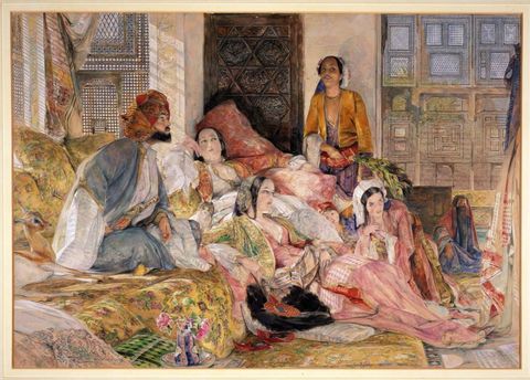 Watercolour. Four women, two men, and a child look at something out of our view to the right. One man sitting cross-legged on a couch wears an elaborate turban and voluminous robes. Three of the women recline and lounge near him. The women have pale skin and the two men more tanned complexions.