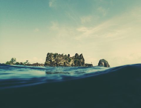 A rocky outcropping with sheer sides in the distance is suspended over a surging water line, as if we are about to plunge under the surface of dark blue water.