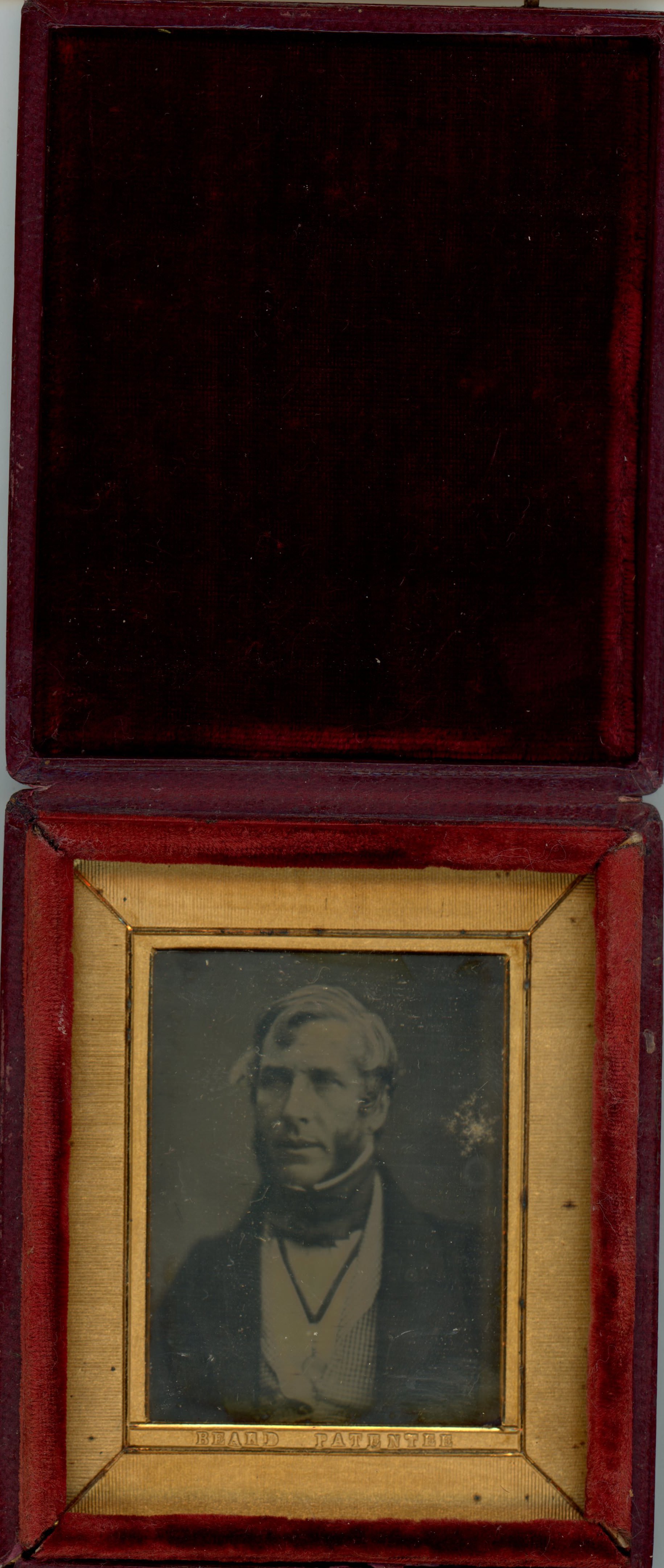 Daguerreotype in an open case. A pale-skinned, light-haired man with thick mutton chops looks off to our left. He is framed in the rectangular opening of a gold mat, which his incised with lines to create a secondary frame. The case flips up, and the cover is lined with dark fabric.
