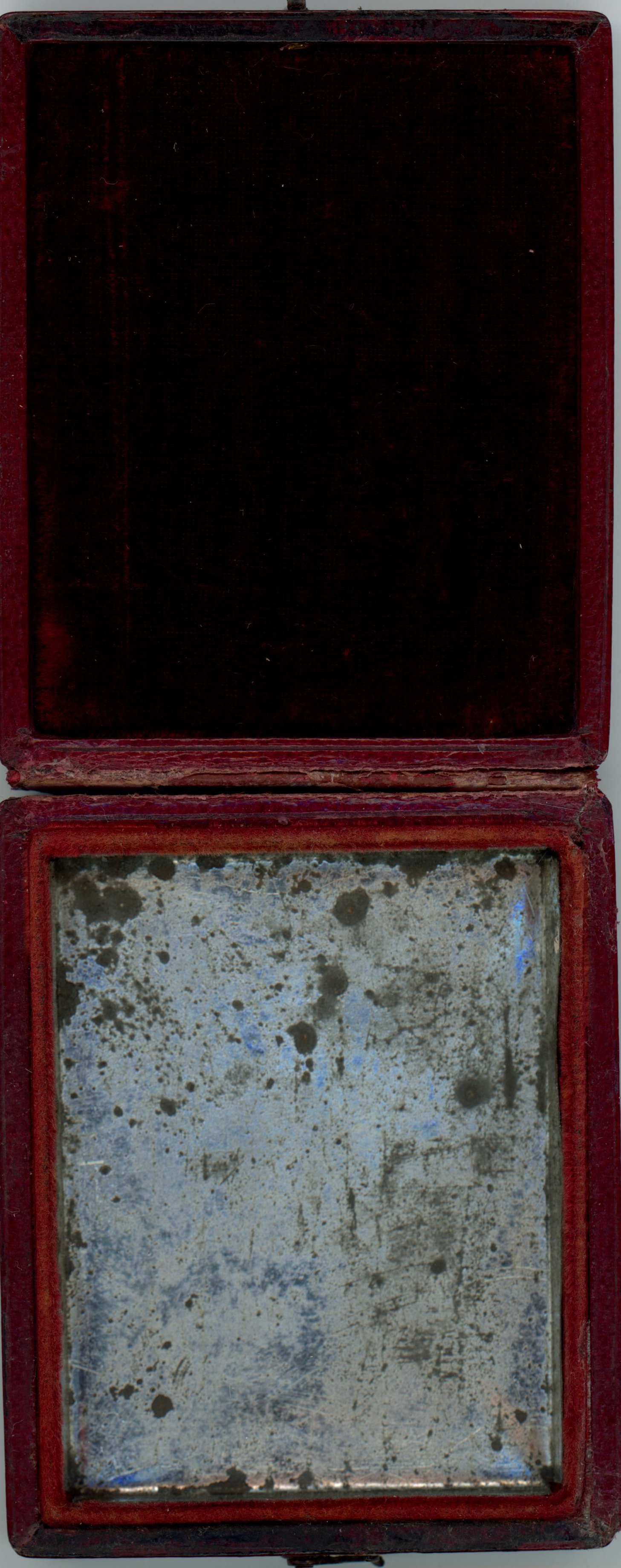 Case. Open daguerreotype case with black fabric in the top is lined with mottled silvery tin in the bottom.